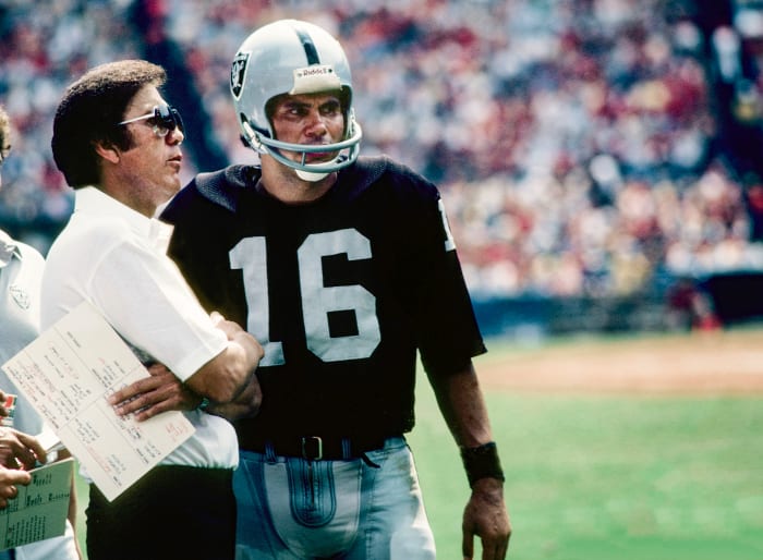 Tom Flores and Jim Plunkett talk on the sideline during a game in 1982